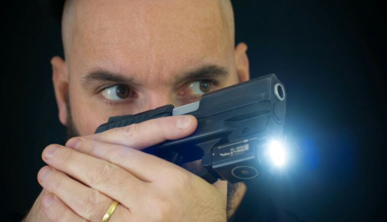 Man with mostly shaved hair aiming with a taser gun close to his face.