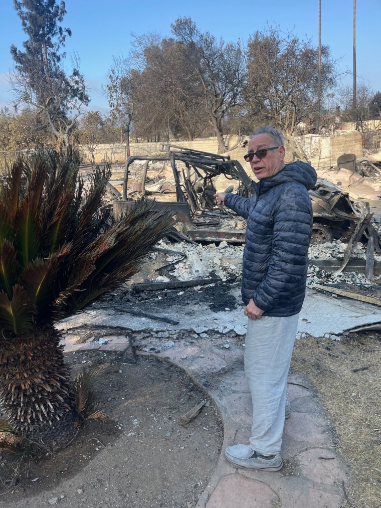 Antonio Antonetti pointing at his neighbor's burned property bordering his backyard outside