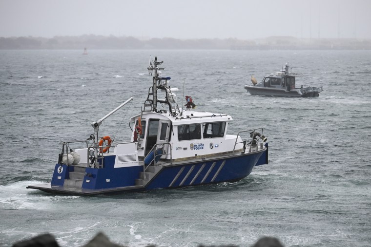 A San Diego Harbor patrol and a U.S. Navy boat work along the shore