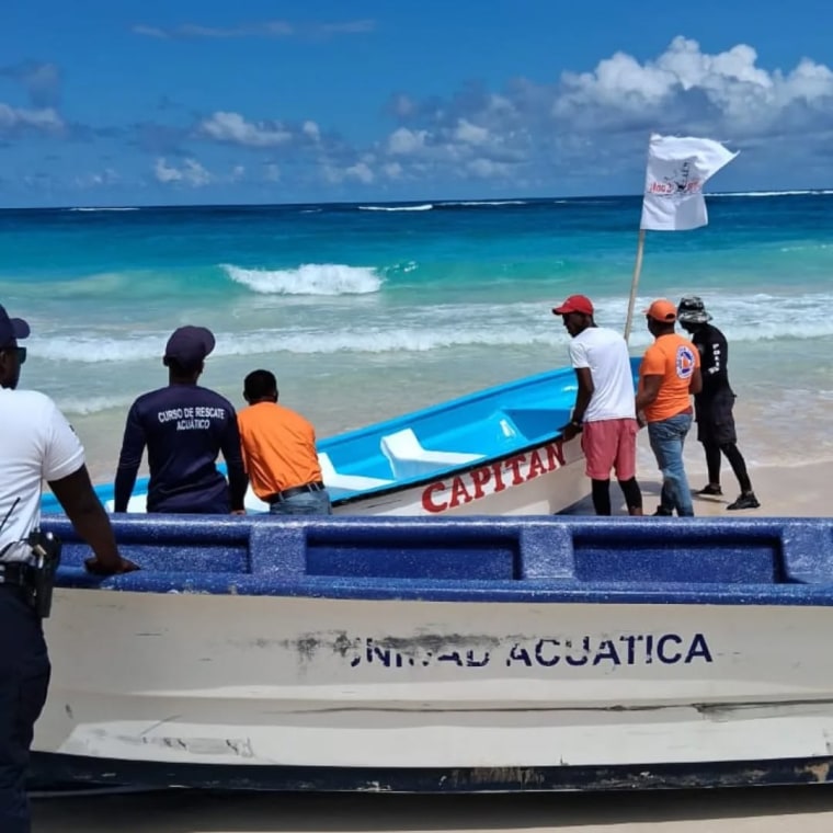 People gather in a group to search on a beach shore, they carry boats to the water