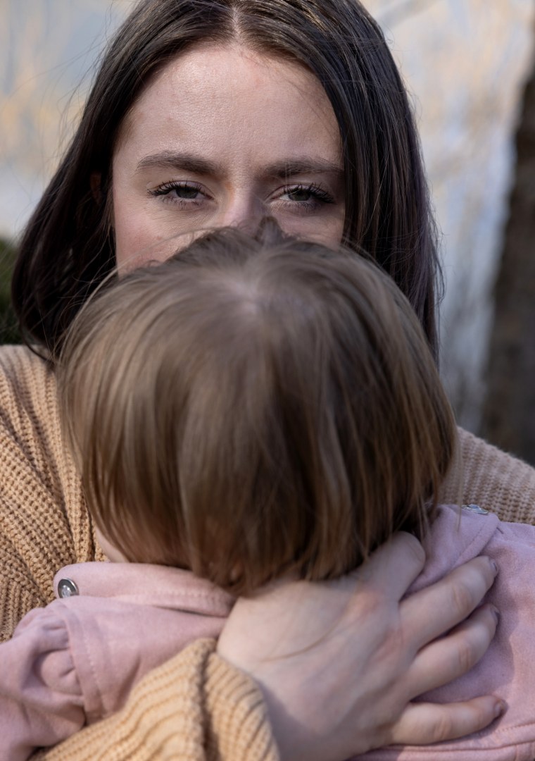 Saige Dahmen holds her daughter while looking into the camera. Half her face is covered by her daughters head.