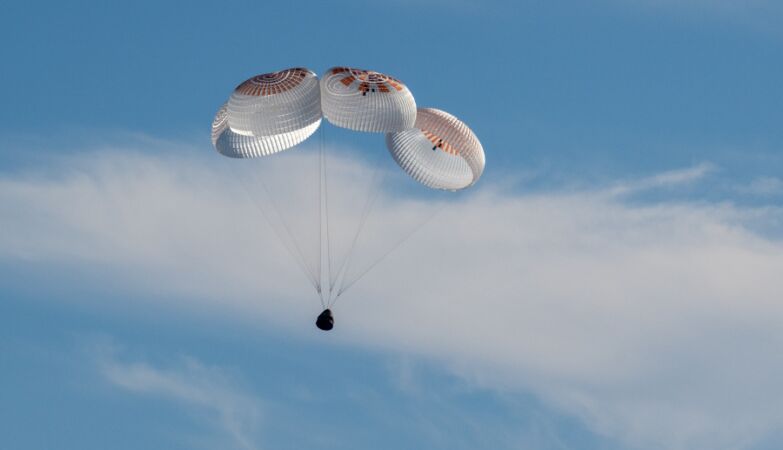 Spacex capsule with parachutes in the blue sky, in the return to the land of NASA astronauts trapped in space.