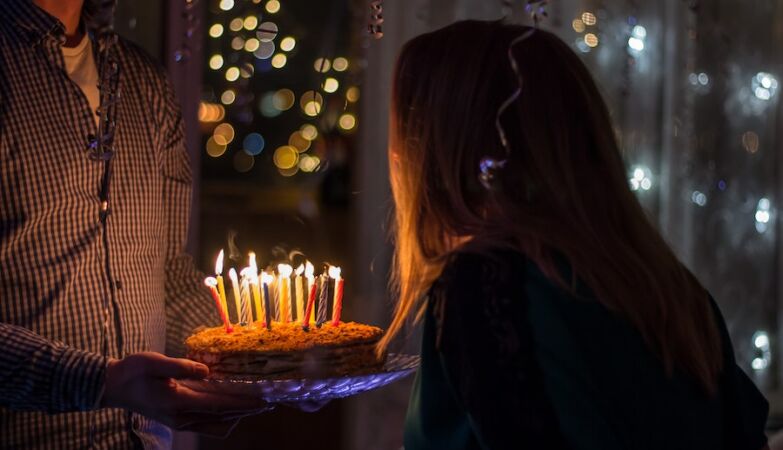 A man holding on a birthday cake while a young man blows his candles