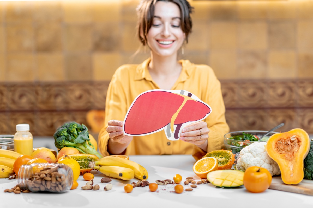 Color photo of a woman in a yellow blouse, holding a drawing that resembles a human organ, surrounded by food, sits on a table. - Metropolises.
