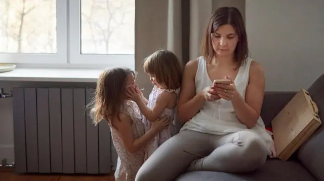 Mother with two daughters at home using her cell phone.