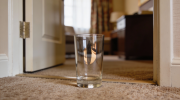 Copo de vidro no chão de um quarto de hotel. Crédito: Freepik AI