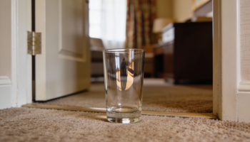 Copo de vidro no chão de um quarto de hotel. Crédito: Freepik AI