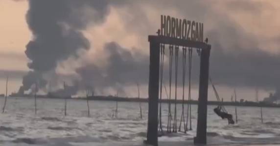 Young Iranian woman filmed riding a swing near the Strait of Hormuz with smoke from a drone attack in the background