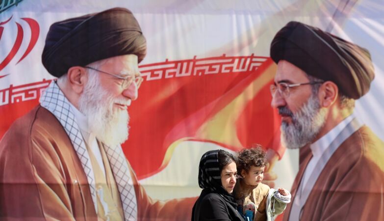 An Iranian woman and child walk past a poster featuring the late Supreme Leader Ayatollah Ali Khamenei (left) and his son, the now Supreme Leader Ayatollah Mojtaba Khamenei (right), in Tehran, Iran.