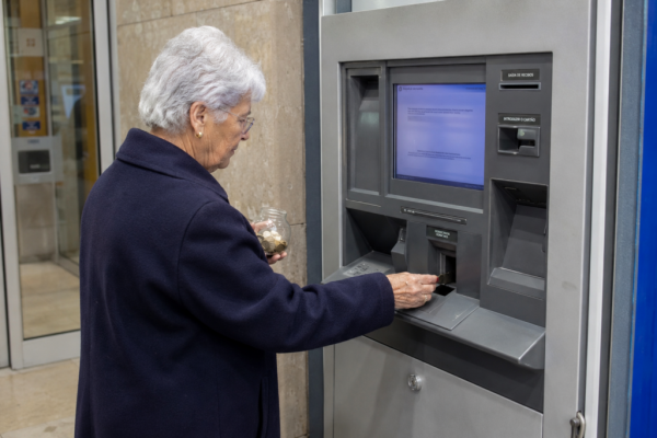 Idosa a depositar moedas. Crédito: Foto AI