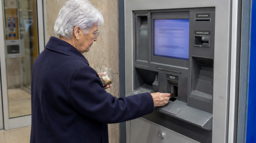 Idosa a depositar moedas. Crédito: Foto AI