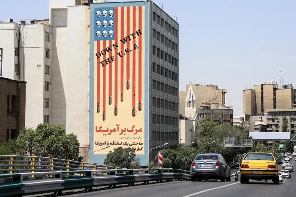 Passengers walk across a bridge near a building with an iconic anti-US mural in Tehran on June 22, 2025 (AFP/Getty Images)