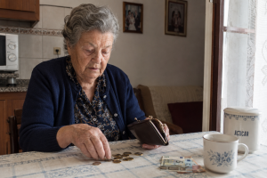 Mulher idosa a organizar moedas e notas. Crédito: Foto AI
